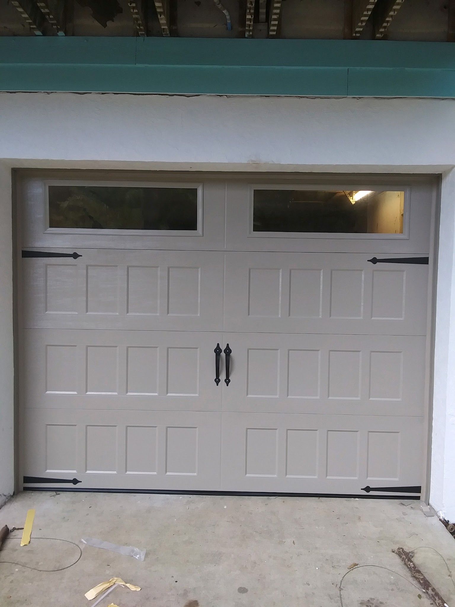 Tan carriage-style garage door with black hardware, newly installed on a white house