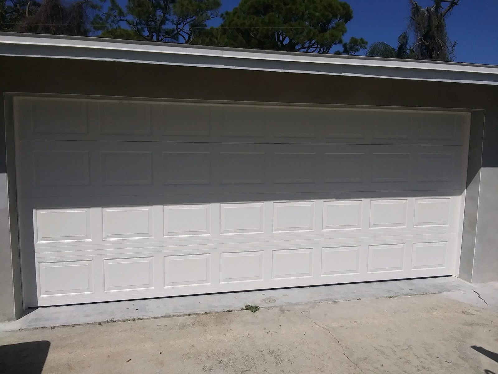 White raised-panel double-car garage door on a light stucco house