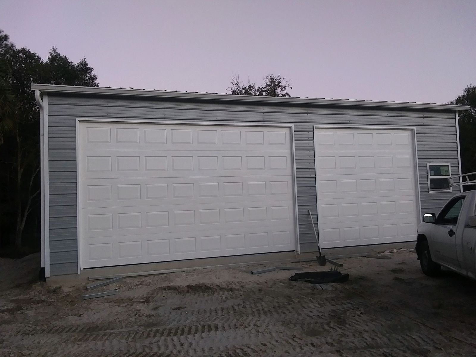 White double-car and single-car garage doors installed on a gray metal building