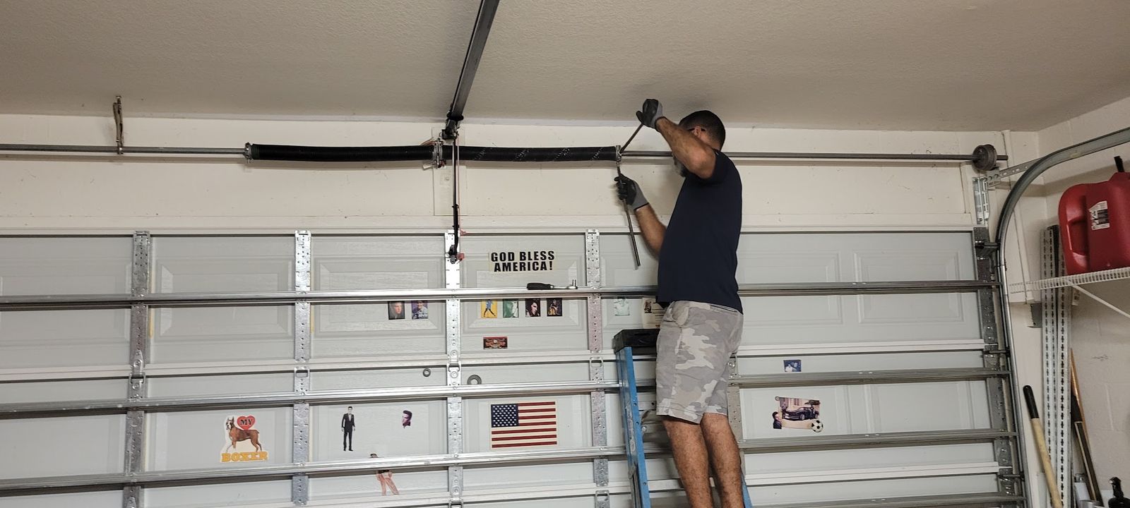 Technician on a ladder winding a garage door torsion spring