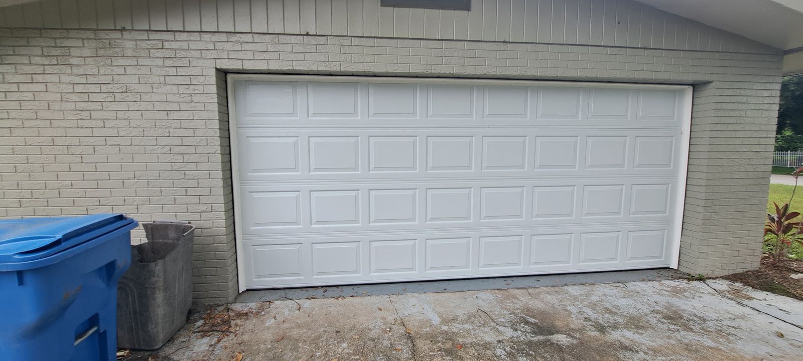 White double-car raised-panel garage door in a light brick wall
